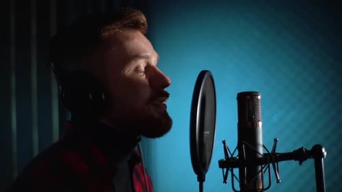 Closeup Face of Man Singer in Headphones Singing Song Into the Microphone at Music Record Studio