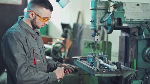 Man Measuring Metal Part with Calipers in Workshop