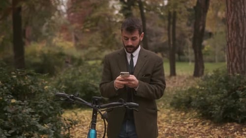 Handsome young man with electric bicycle using mobile phone in the autumn park