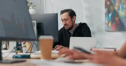 A Man Who Works in an Office Takes a Break From Work Sits in Front of a Computer Smiles at the
