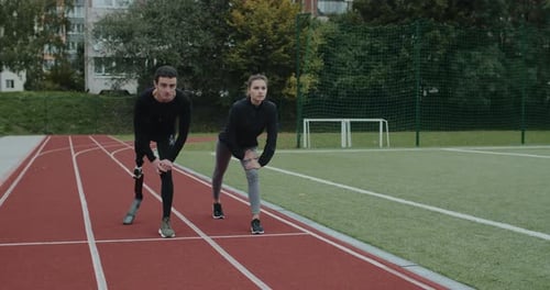 Athlete with Prosthetic Leg Running with Woman on Track