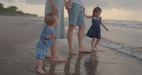Young Family of Four Stand on the Sea Coast, Holding Hands Together