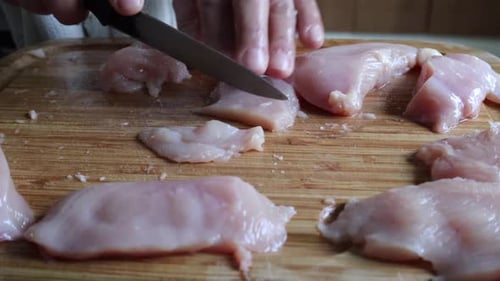 Kochen Sie das Schneiden von frischem Hühnerfleisch in Streifen mit einem scharfen Messer im Holzbrett - hoher Winkel, Nahaufnahme