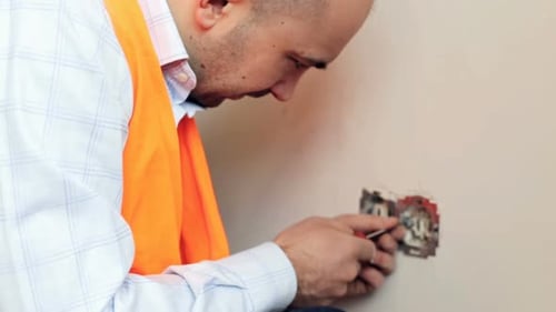 Electrician Repairs Electrical Outlet With a Screwdriver