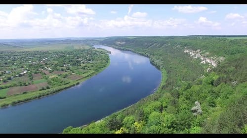 A wide blue river flows between rocks with trees and countryside with long fields