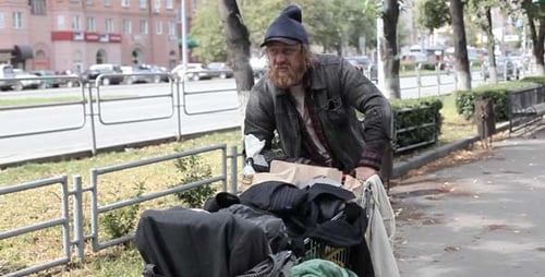 Man Pushing Cart with Belongings Down Sidewalk