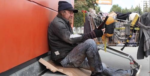 Man Drinking Next to Shopping Cart of Belongings