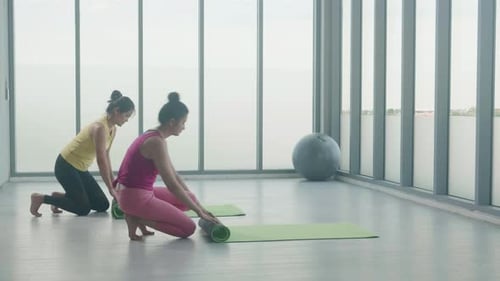 Two Women Rolling Yoga Mats Indoors