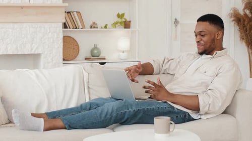 Man Relaxing on Couch, Video Conferencing on Laptop