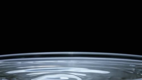 In Zeitlupen-Makroaufnahme fällt ein Wassertropfen auf die Wasseroberfläche