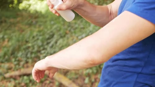 Adult Sprays Insect Repellent On Arm Outdoors