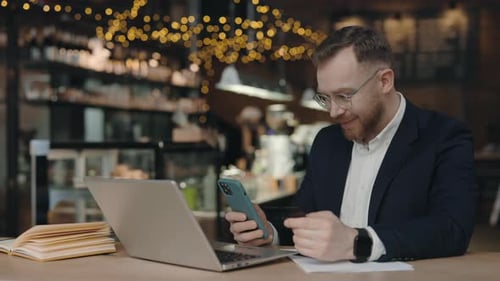 Man Using Phone and Credit Card at Cafe
