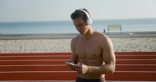 Muscular Man Dancing with Phone on Beach Track