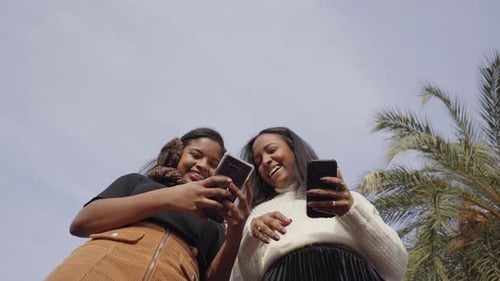 Two Women Using Phone Outdoors in Urban Setting