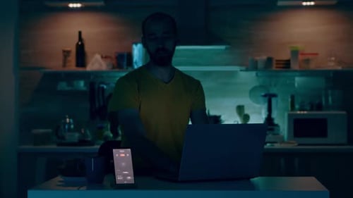 Man Working on Laptop Computer in Kitchen at Night