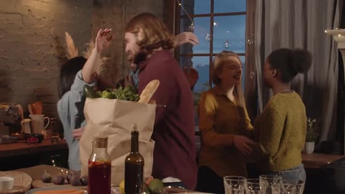 Friends Gather in Warmly Lit Kitchen with Groceries