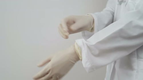 Adult Putting on White Latex Gloves in Hospital