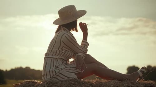 Woman Sitting on Hay Bale at Sunset