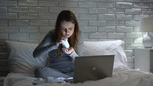 Woman Examines Pills with Laptop in Bedroom at Night