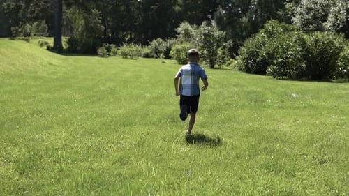 Attractive Boy Runs Along the Grass in the Park Having a Good Mood