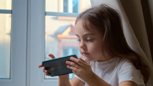 Girl Plays Game on Smartphone at Home