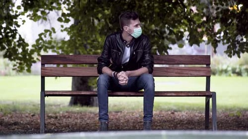 Ein junger cooler Mann in Jeans, weißem T-Shirt und schwarzer Kunstlederjacke, der einen grünen Covid-19-Fa trägt