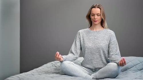 Blonde Woman Meditating on Bed in Lotus Position