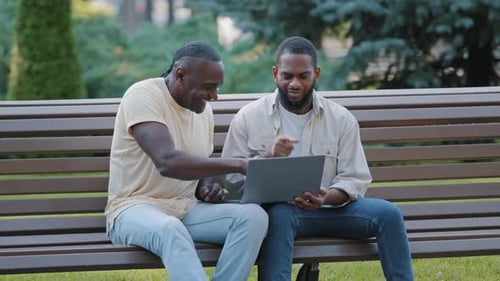 African American Black Male Friends Sitting in Park Looking at Computer Screen