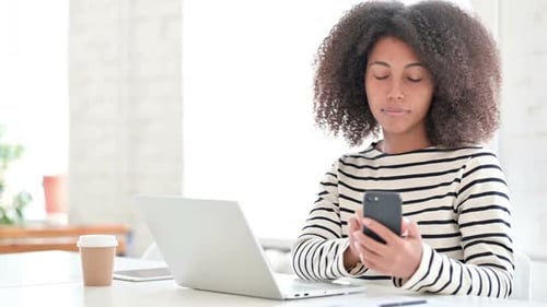 Woman Using Smartphone at Desk in Bright Office