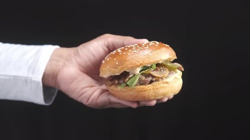 Hand Holding Beef Burger on Table Close Up