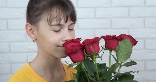 Girl Smells Red Roses in Front of Brick Wall