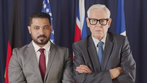 Two Men in Suits Stand Before Flags