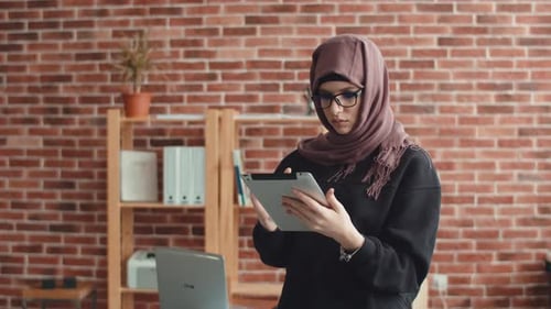 Una mujer musulmana escribe en una tableta digital y mira a la cámara. Una mujer joven en un hiyab