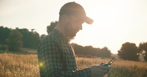 Closeup shot showing male operator flying drone between golden fields in wilderness.