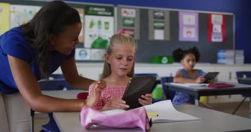 Teacher Helping Young Girl with Tablet in Classroom