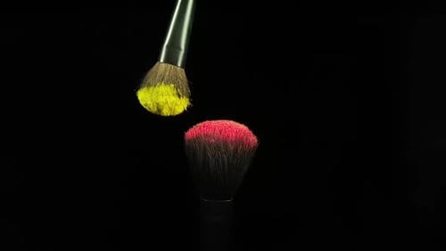 Makeup Brushes Touch Each Other on Black Dark Background and Small Particles of Color Cosmetics