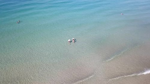 Turquoise clear water, light waves and free beach. People swim in small groups.