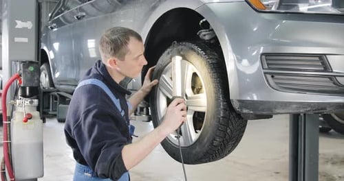 Car Raised On Lift In Car Service, Mechanic Checks Wheels And Brakes