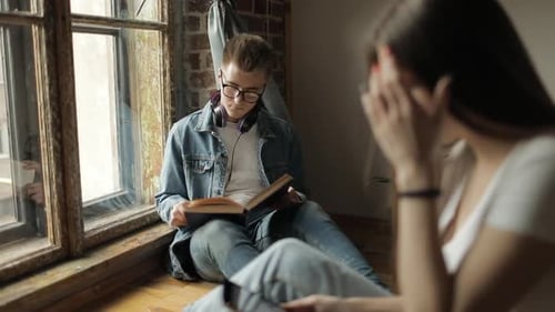 Man Reads Book, Woman Uses Phone in Room