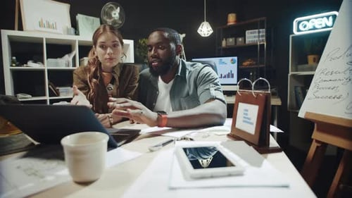 Playful Afro Man and Hipster Girl Talking About Data on Laptop Screen in Office.