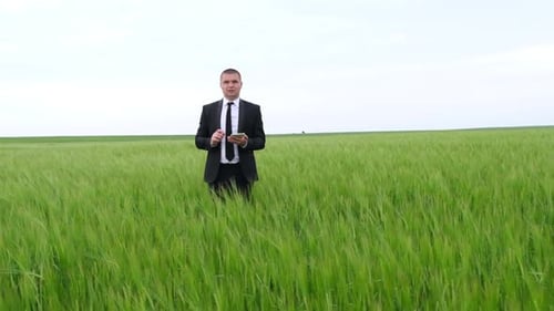 A Young Agronomist Holds a Tablet Computer with a Touchpad on a Green Wheat Field