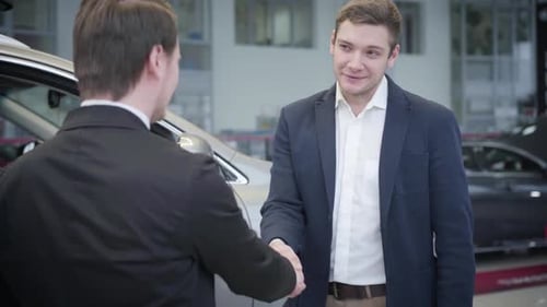 Portrait of Thankful Caucasian Man Shaking Dealer's Hand in Car Dealership