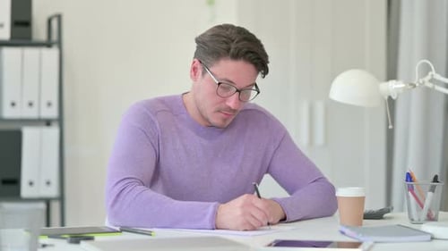 Young Adult Man Writing on Paper at Desk