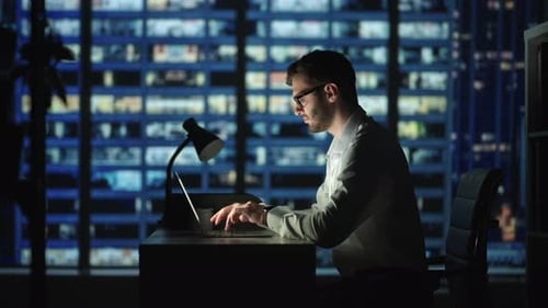 Focused Business Man Working on Laptop Computer Making Notes Sitting at Home Office Desk at Night