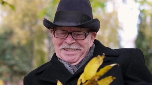 Old and Lonely Grandfather in Glasses and a Black Coat He is Sitting in an Autumn Park on a Bench