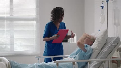 A Darkskinned Female Doctor is Talking to an Old Male Patient Lying on a Hospital Bed Discussing