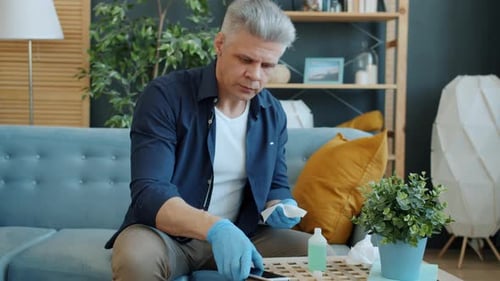 Man Cleaning Smartphone with Sanitizing Wipe in Home