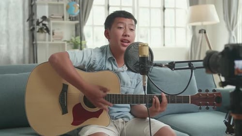 Niño asiático tocando la guitarra y cantando una canción. El chico está transmitiendo
