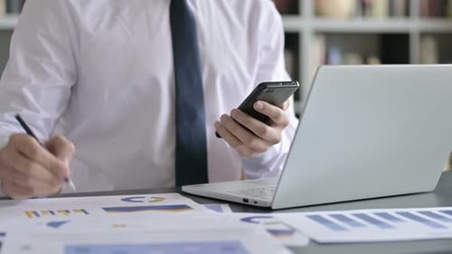 Nahaufnahme eines Geschäftsmannes, der an Dokumenten arbeitet und das Handy benutzt