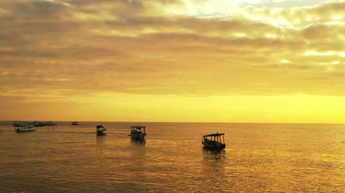 small fishing boats floating in the calm sea with golden colored horizon and reflection of the sky